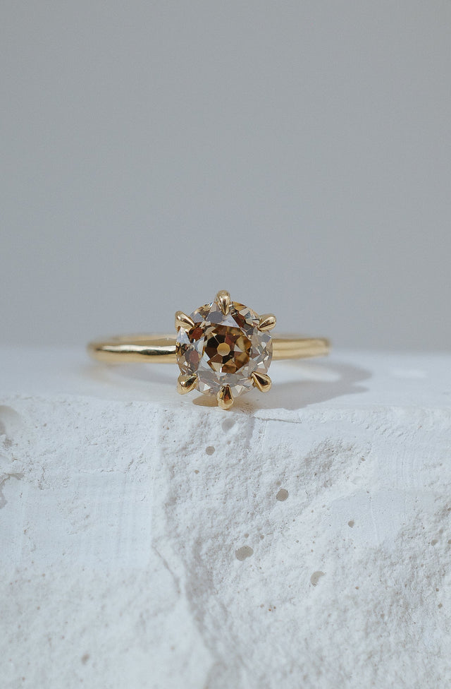 Gold ring with a central gemstone on a textured white surface. champagne round antique cut diamond.