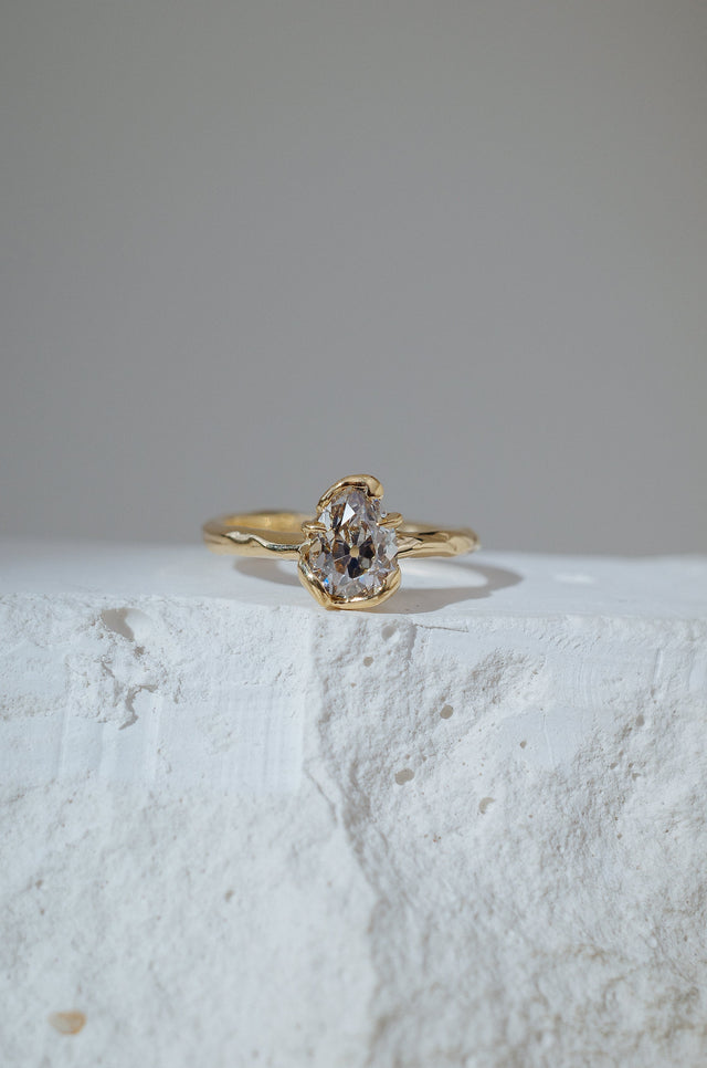 Pear shaped antique diamond with gold swirls and claws holding it.